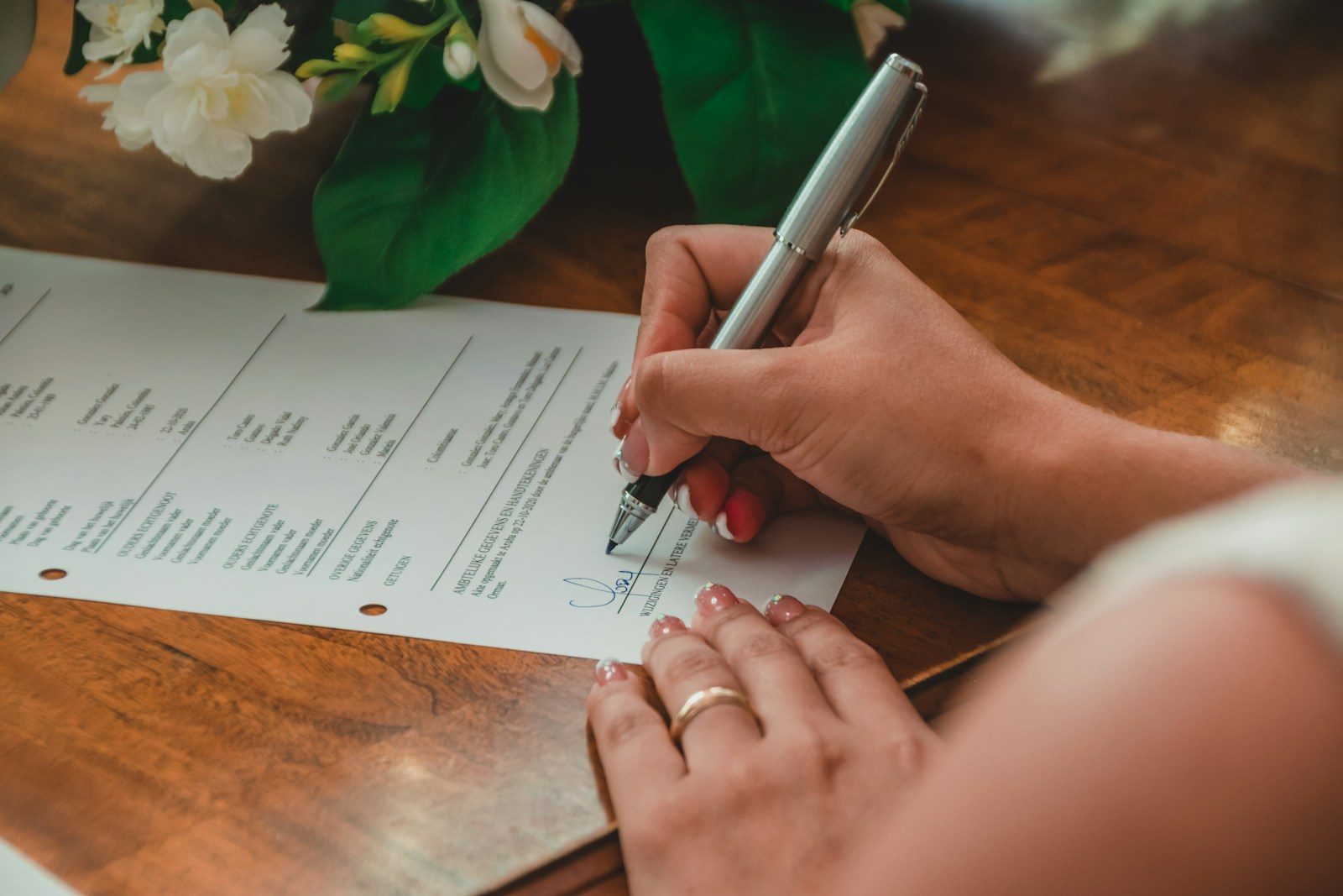 Hand met een zilveren pen die een document ondertekent op een houten tafel