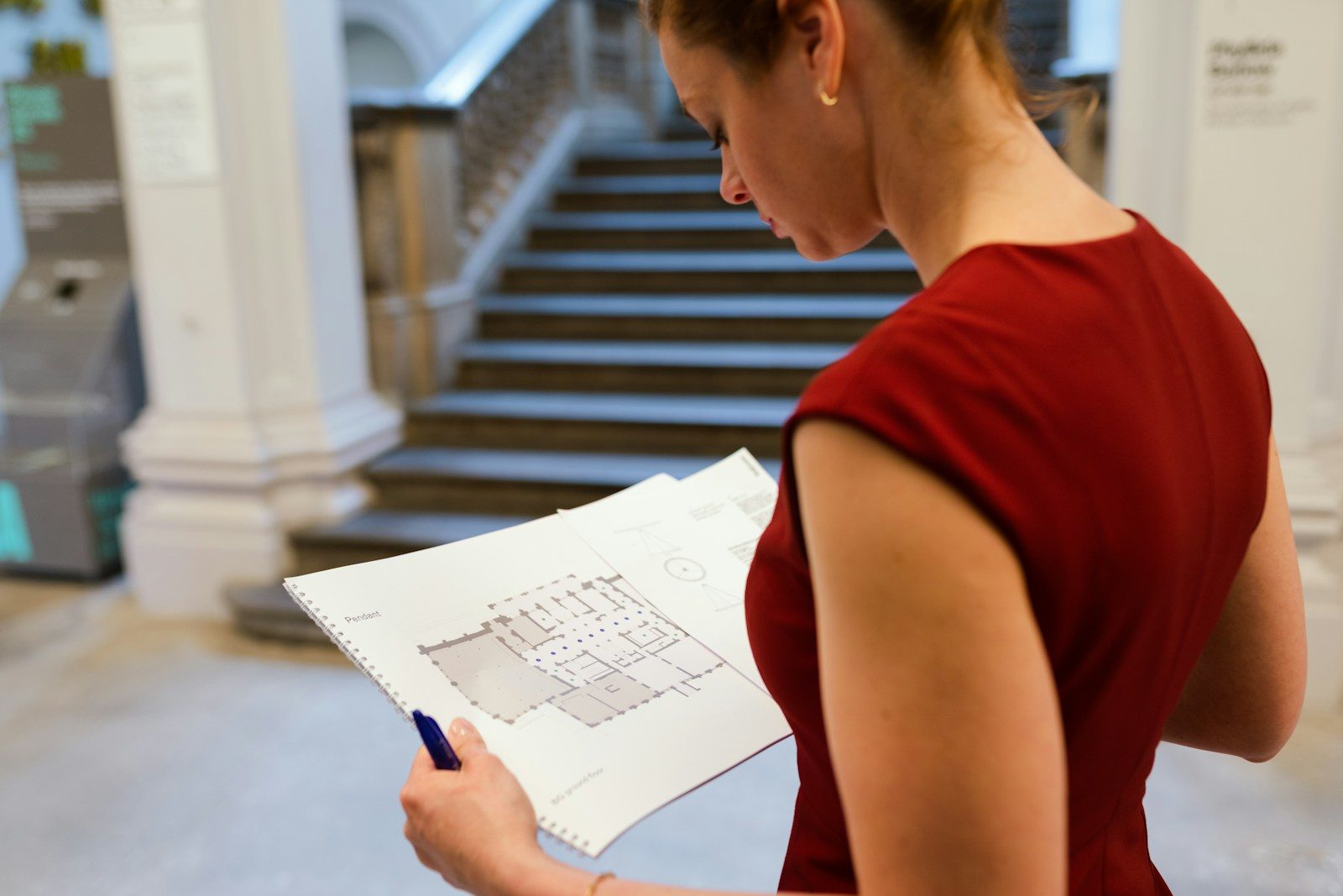 Vrouw die in een hal met een trap een bouwplan leest