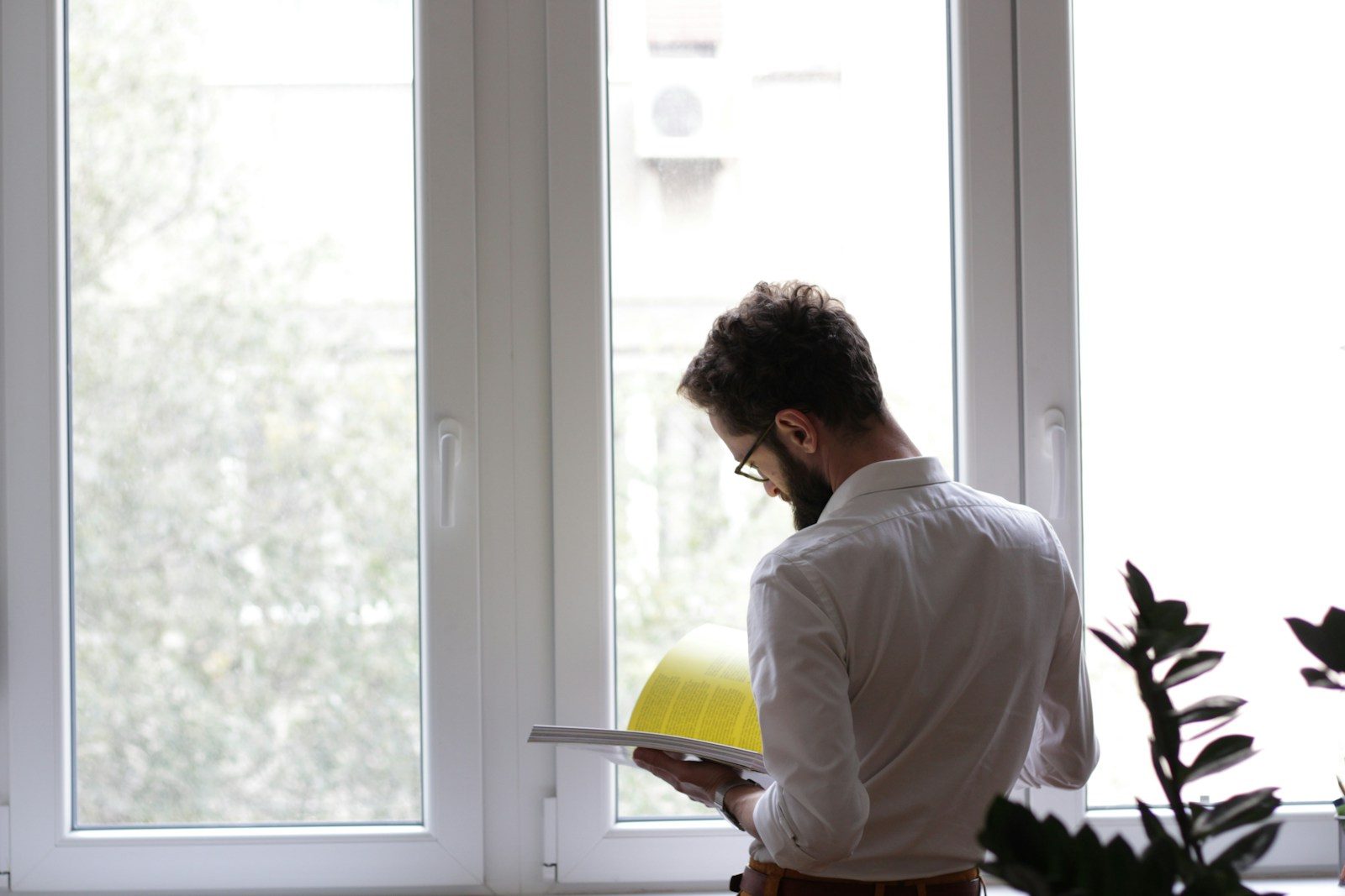 Man met een tablet en een gele bouwhelm bij een groot raam